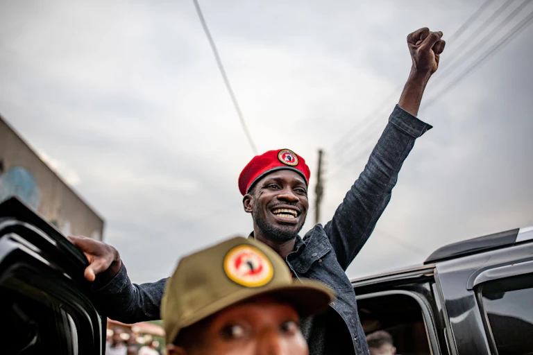 Robert Kyagulanyi Ssentamu. smiling and wearing a red beret, raises his fist in the air