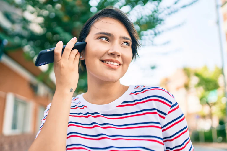 Una mujer joven escucha un mensaje de voz acercando a su oído su teléfono móvil.