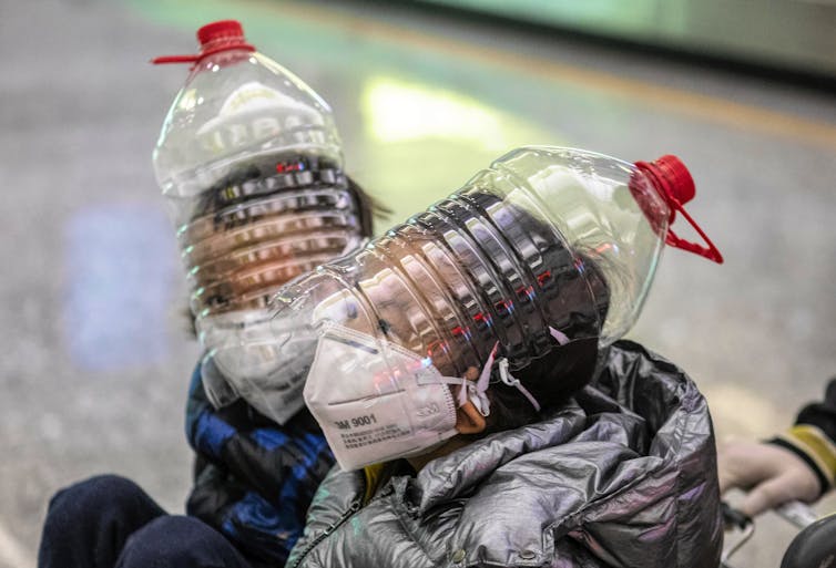 Boys wearing protection masks, gloves and modified water bottles over heads.