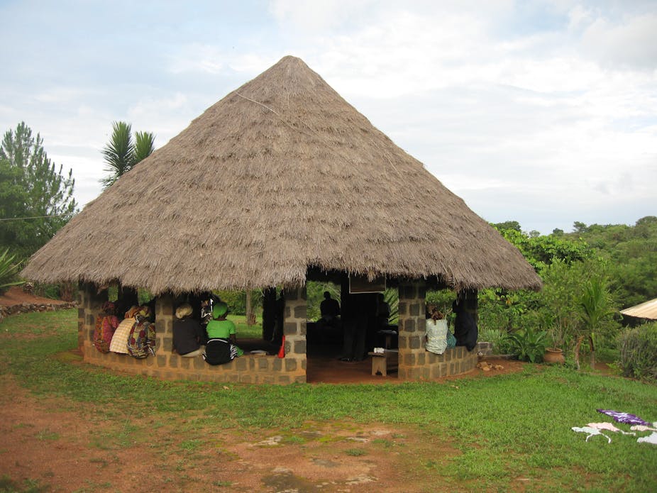 Community members meeting in a building with a thatched roof