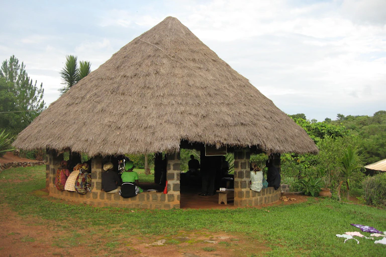 Community members meeting in a building with a thatched roof