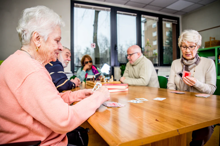 Un grupo de personas mayores juega y conversa alrededor de una mesa.