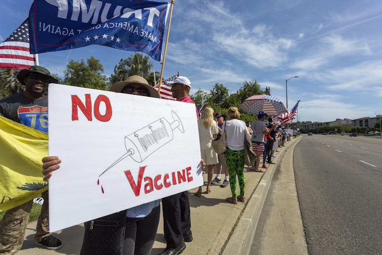 People protesting pandemic restrictions and rules, one holds a 'No vaccines' sign