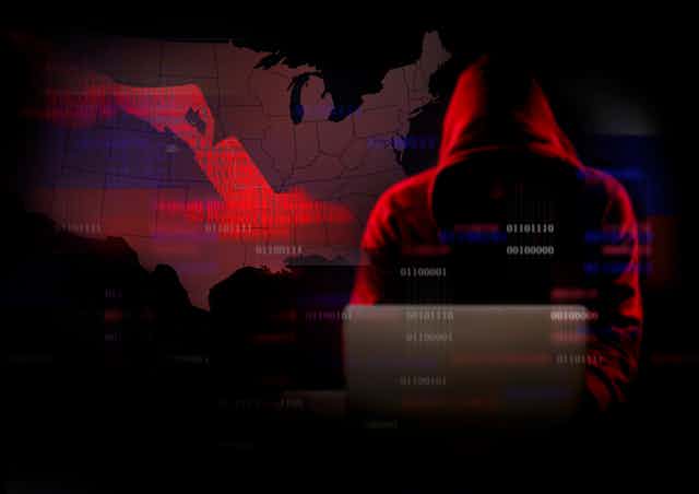 Hooded man on laptop codes in front of map of USA
