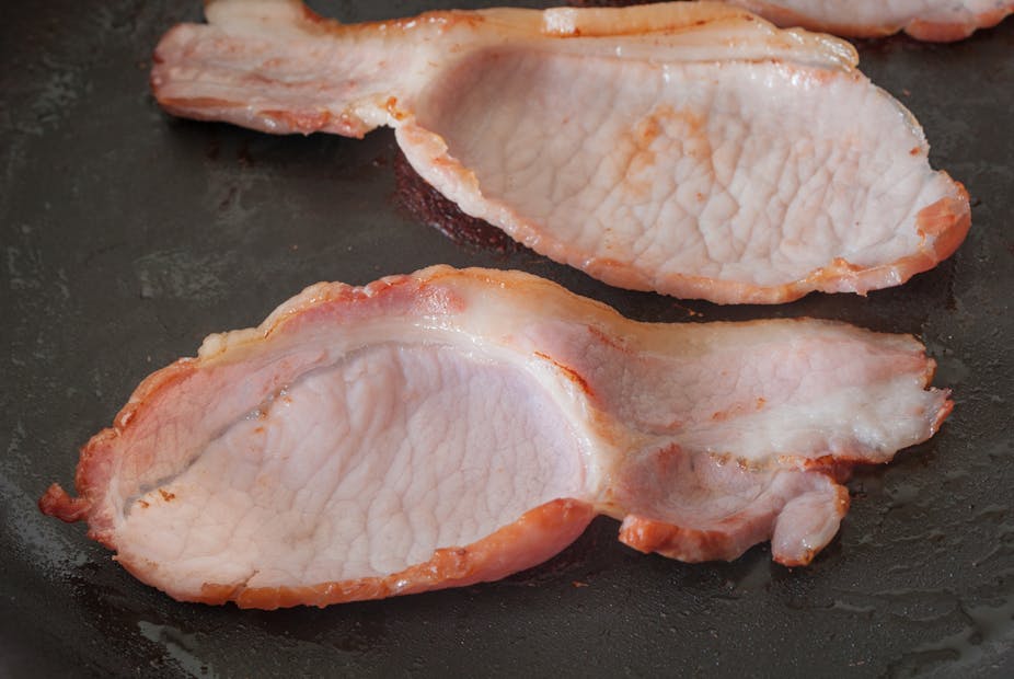 Lightly-browned back bacon in a pan.