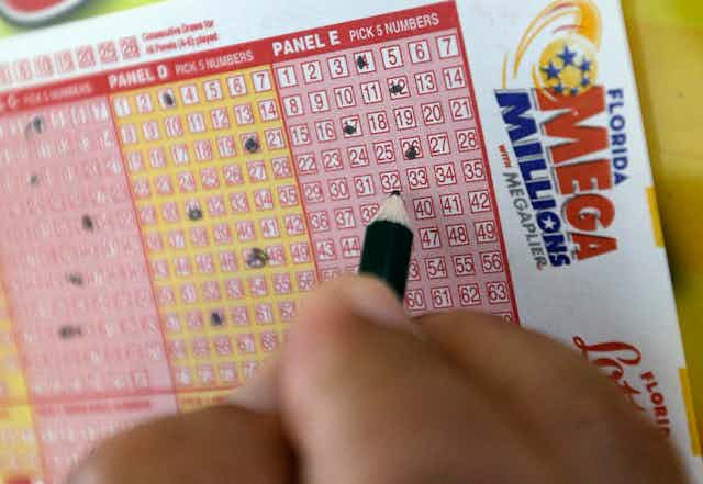 A hand filling out a Mega Millions lotto card.