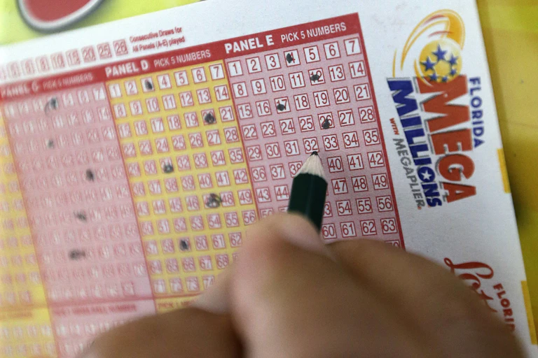 A hand filling out a Mega Millions lotto card.