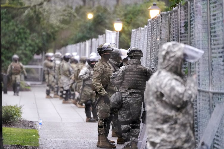 National Guard troops stand along a chain link fence.