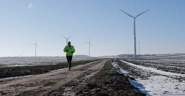 A jogger passes snow-covered fields with wind turbines in the background.