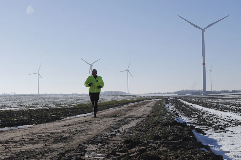A jogger passes snow-covered fields with wind turbines in the background.