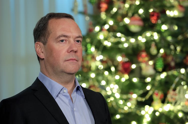 Dmitry Medvedev, a middle-aged Russian politician, poses in front of a Christmas tree.