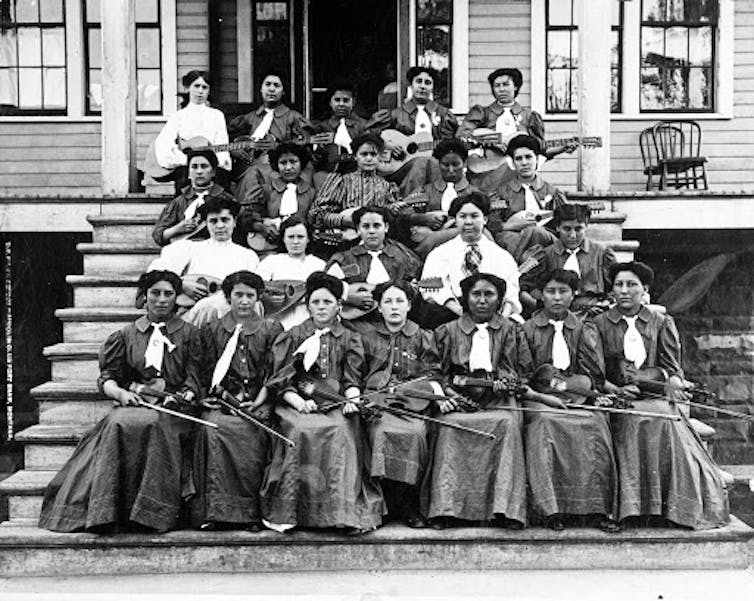 Black-and-white image of Native students in Victorian dresses holding violins