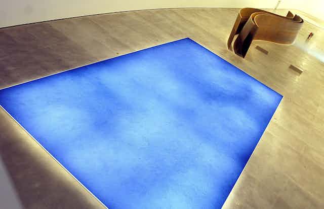A blue painting by Yves Klein underlit on the floor of an art gallery.