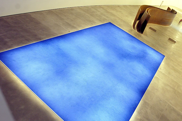 A blue painting by Yves Klein underlit on the floor of an art gallery.