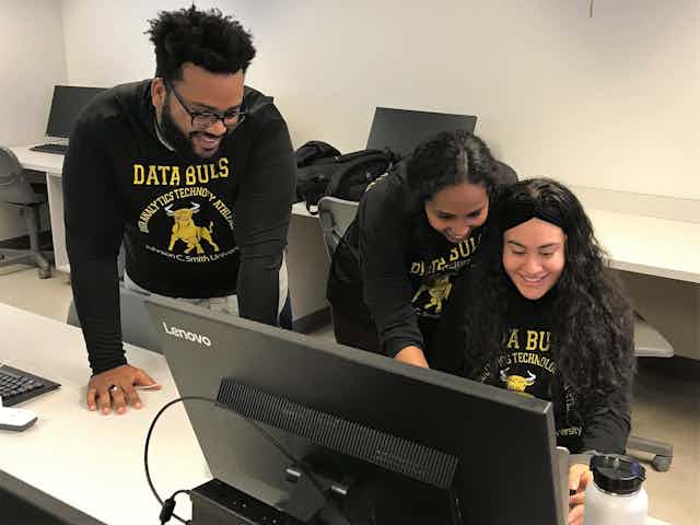 Three college students wearing sweat shirts that say "DATA BULLS" are at a computer.