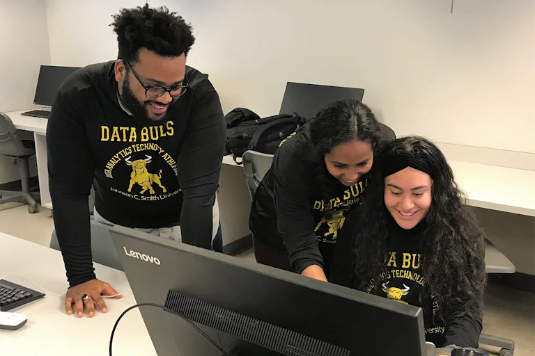 Three college students wearing sweat shirts that say "DATA BULLS" are at a computer.