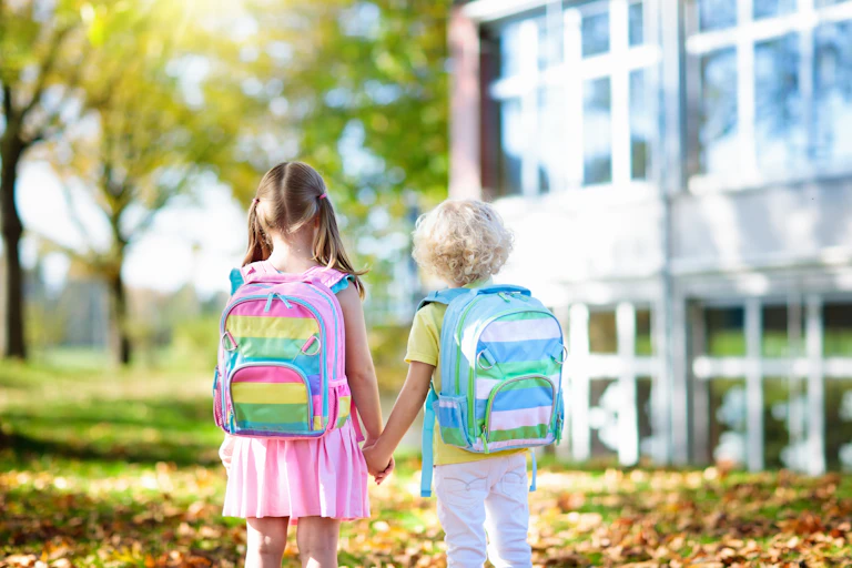 Two children holding hands in front of a school building.
