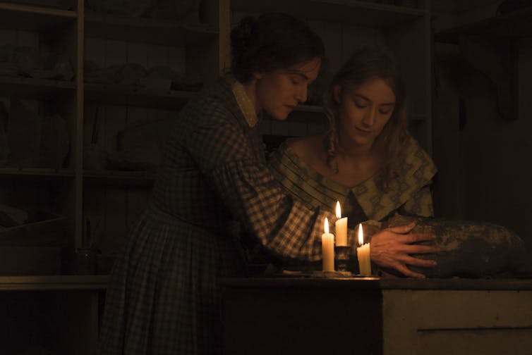 Anning and Murchison look over a rock by candlelight.