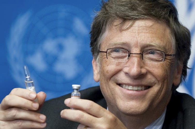 Bill Gates in front of UN logo holding a vaccine.