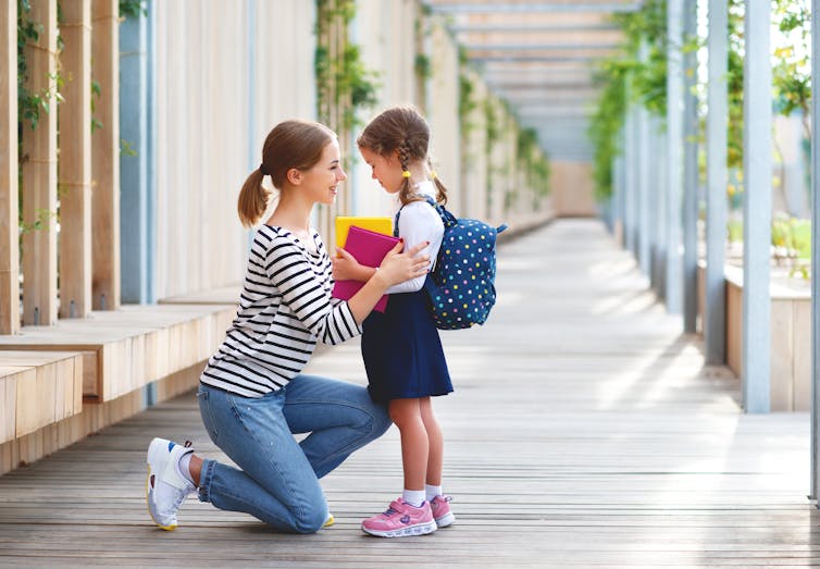 Mother talking to her schoolgirl kid and smiling in the school corridor.