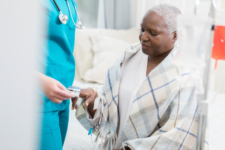 A nurse monitors a woman using a pulse oximeter.