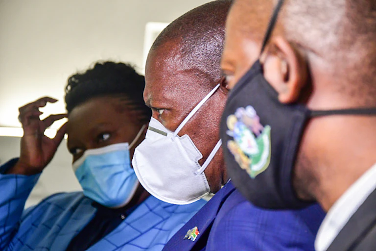 Two men and a woman wearing face masks and staring at something intently.