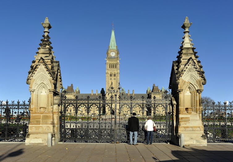 Two members of the public look through the closed gates of Parliament Hill, Canada's national parliamentary estate.