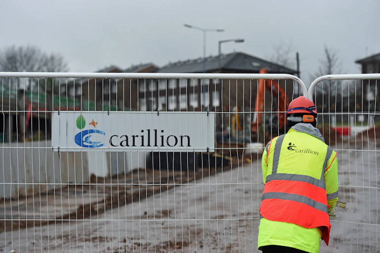 Workman closing barrier with a Carillion sign on it.