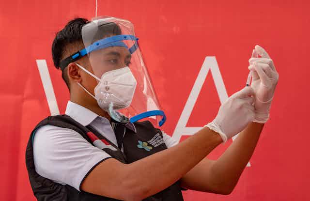 A medical worker in Indonesia loading a syringe with vaccine fluid