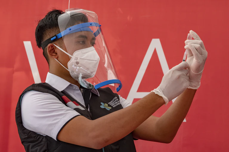 A medical worker in Indonesia loading a syringe with vaccine fluid