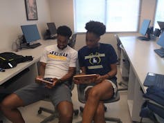Two African American students use iPads in a computer room.