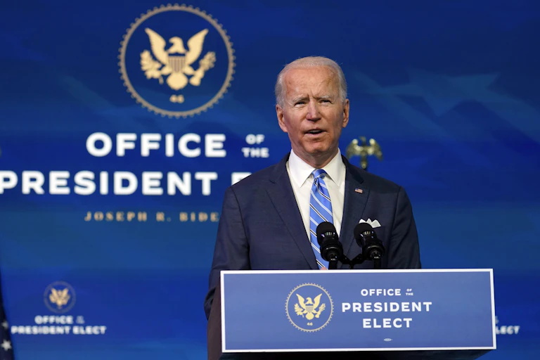Joe Biden in a blue suit and tie speaks behind a podium that says Office of the President Elect.