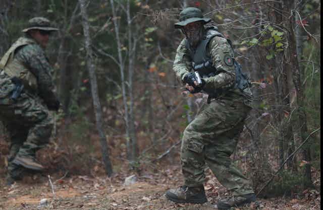 Men in military fatigues run with weapons in the woods