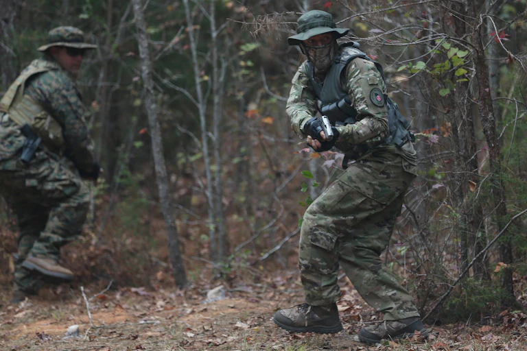 Men in military fatigues run with weapons in the woods