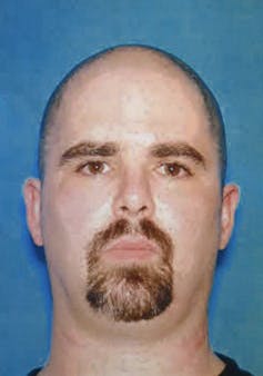 Head shot of a balding white man with a goatee against a blue background