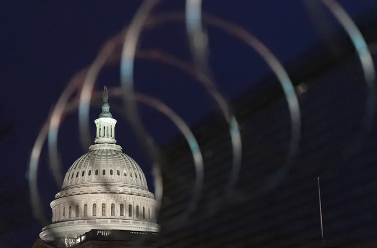 The U.S. Capitol dome is seen in the darkness behind razor wire.