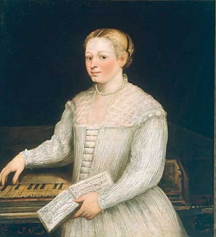 A woman stands looking at the viewer, her hand draped over a piano.