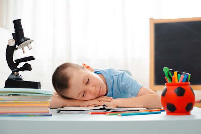 Boy sleeping at the desk with microscope and learning materials around him.
