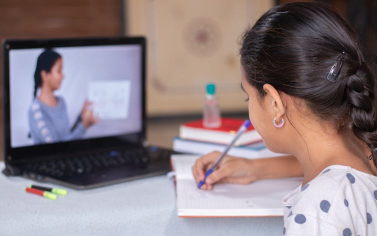 Girl learning at home with computer in front of her, and teacher showing something.