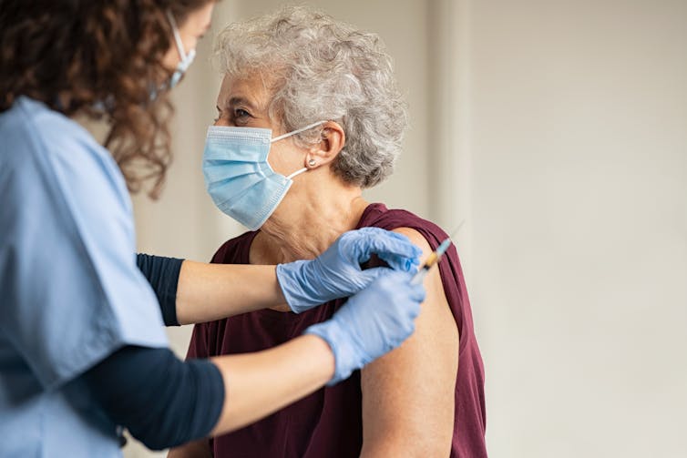 A nurse administers a vaccine to an elderly lady wearing a mask.