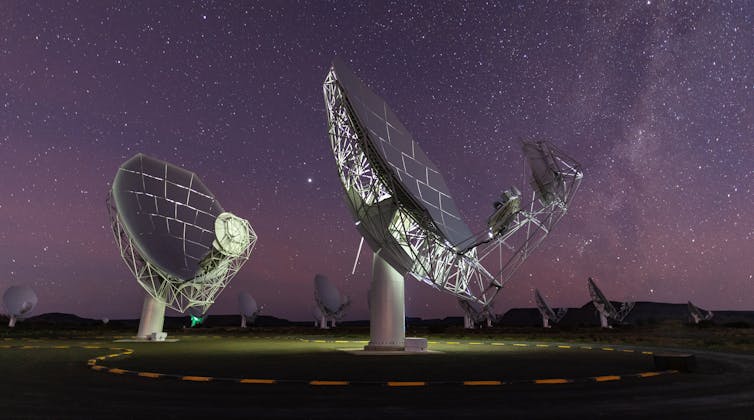 Two massive satellite dishes are pointed up towards the night sky