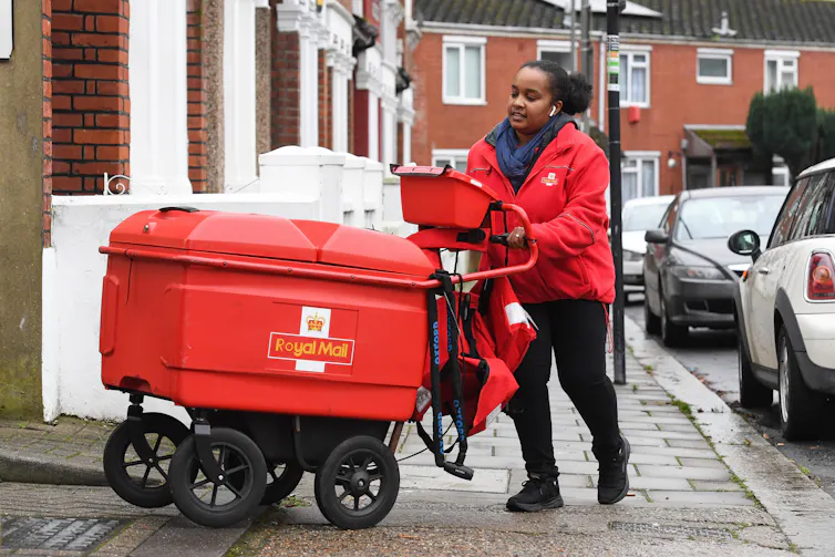 Royal Mail woman postie pushing trolley full of post on her rounds during lockdown.
