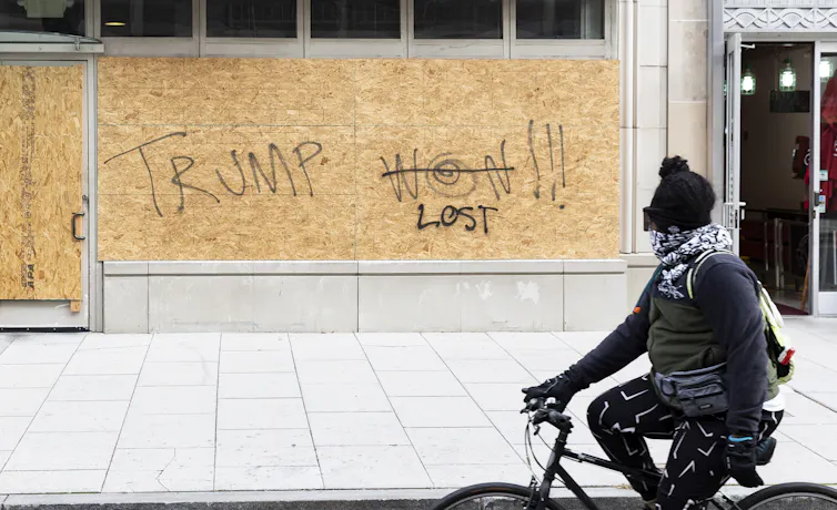 A cyclist looking at graffiti that originally said 'Trump won!' but has been changed to read 'Trump lost'.