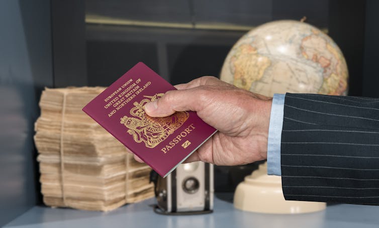 Senior executive hand holding UK passport against blurred background of world globe and camera