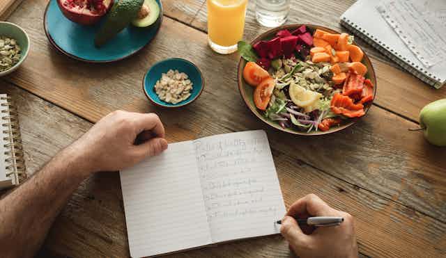 A man writes in a diary on a table with healthy food.