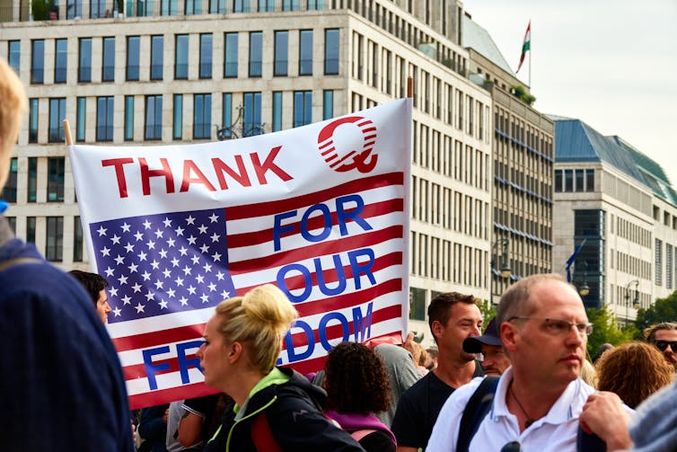 Protestors with flag showing US flag and QAnon logo