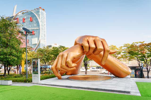 Escultura de unas manos doradas en una postura de la coreografía del Gangnam Style en medio de un parque. 