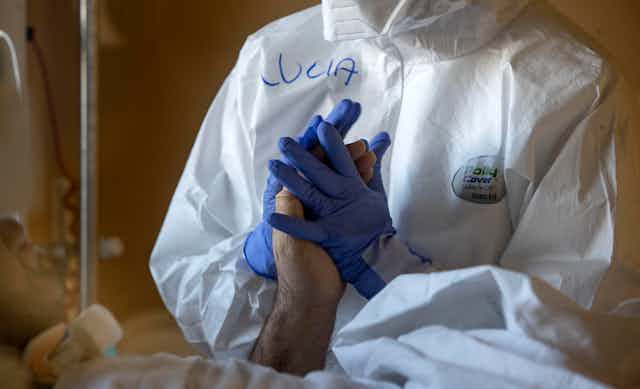 A hospital worker wearing PPE holding a patient's hand