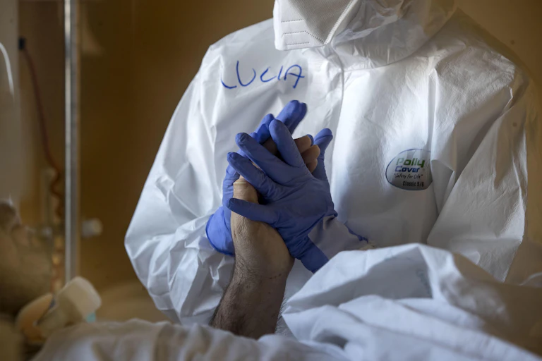 A hospital worker wearing PPE holding a patient's hand