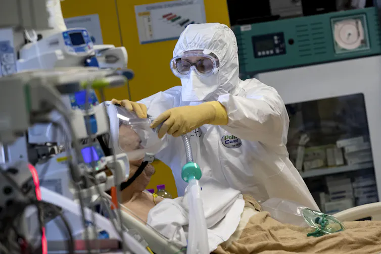 An Italian health worker in PPE adjusting a COVID-19 patient's breathing apparatus
